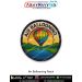 Bright, colourful circular patch showing a multi-colour hot air balloon floating above a lake with surrounding green hills and orange sunset sky, finished with a black merrow border — ideal for travel and adventure lovers, ballooning fans, bikers, and col